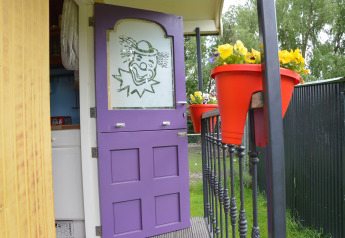 Lilla dør med klovnemotiv i mobilhjem Pipowagen 'de Weideblick', Holland, blomster i røde potter.