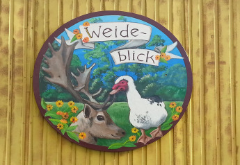 Letrero pintado con un reno y un ganso, texto: 'Weide-blick', sobre pared amarilla, Pipowagen en los Países Bajos.