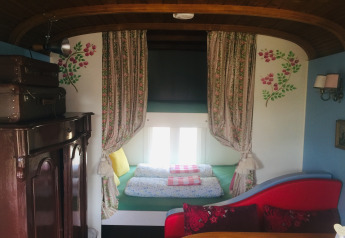 Interior de la casa rodante Pipowagen 'de Weideblick' en Países Bajos con cama acogedora y cortinas florales.