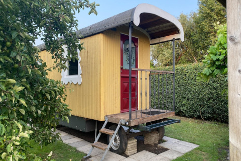 En gul mobilvogn med rød dør og dekorativt vindue i grøn have, Pipowagen de Weideblick i Holland.
