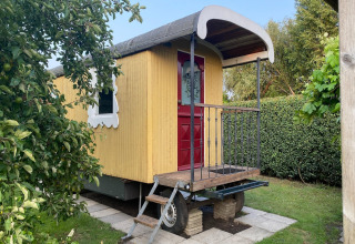 Gelber Wohnwagen mit roter Tür und weißem Fenster, Pipowagen de Weideblick in den Niederlanden.