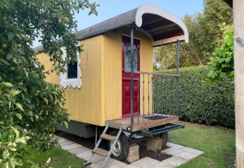 Casa móvil amarilla con puerta roja y ventana blanca, Pipowagen de Weideblick en los Países Bajos.