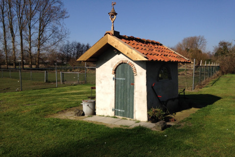 Kleines Häuschen mit rotem Ziegeldach und grüner Tür auf einer Wiese bei Pipowagen 'de Weideblick', Niederlande.