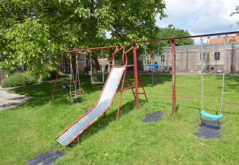 Parque infantil con tobogán y columpios en césped junto a Pipowagen 'de Weideblick', Países Bajos, en un día soleado.