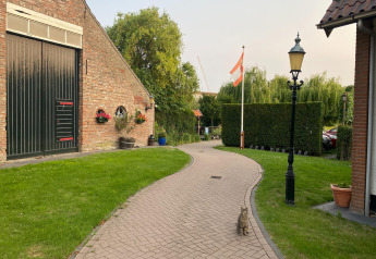 Sti foran mobilhjem Pipowagen 'de Weideblick' i Holland, med kat, have og flag i baggrunden.