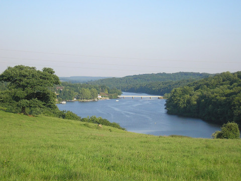 Uitzicht op een rivier met brug, groene weiden en bossen bij Glamping des 2 Marguerites in Normandië.