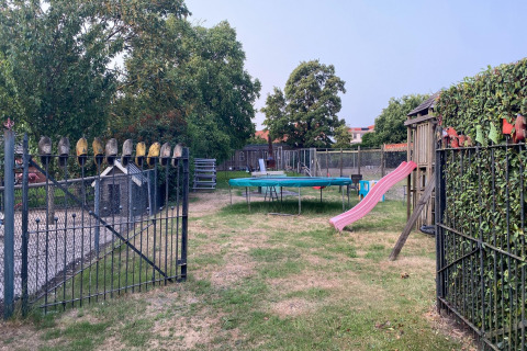 Parque infantil con tobogán, trampolín y cerca decorada con zuecos en Pipowagen de Weideblick, Países Bajos.