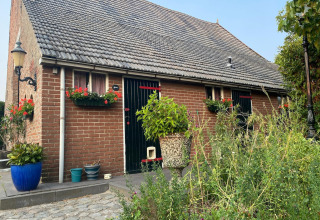 Backsteinhaus mit Blumen und Pflanzen im Vordergrund, Mobilheim Pipowagen de Weideblick in den Niederlanden.