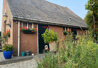 Backsteinhaus mit Blumen und Pflanzen im Vordergrund, Mobilheim Pipowagen de Weideblick in den Niederlanden.