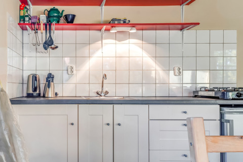 Cucina moderna con mensole rosse, mobili bianchi e piastrelle bianche in una casa vacanze nei Paesi Bassi.