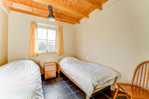 Et lyst soveværelse med to enkeltsenge, træmøbler og store vinduer på Holiday Home 5 Aarde Green Camping Lage Zwaluwe.