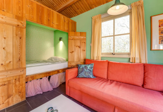 Gemütliches Wohnzimmer mit eingebautem Bett, rotem Sofa und hellgrünen Wänden in Holiday Home 5 Aarde Green Camping Lage Zwaluwe.
