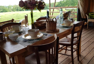 Een gezellige houten eettafel met servies en bloemen, uitkijkend op het groene landschap in Normandië, Frankrijk.