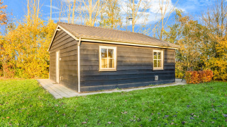 Schwarze Holzlodge bei Holiday Home 5 Aarde Green Camping Lage Zwaluwe mit Rasen und herbstlichen Bäumen.