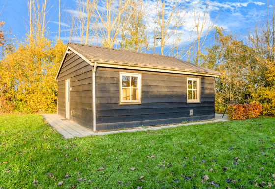 Schwarze Holzlodge bei Holiday Home 5 Aarde Green Camping Lage Zwaluwe mit Rasen und herbstlichen Bäumen.