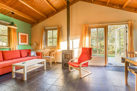 Soggiorno luminoso con arredi rossi, stufa a legna e vista giardino in Holiday Home 5 Aarde Green Camping Lage Zwaluwe.