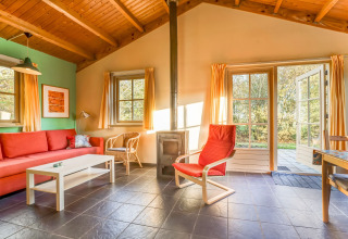 Lichte woonkamer met rood zitmeubilair, houtkachel en tuinzicht in Holiday Home 5 Aarde Green Camping Lage Zwaluwe.