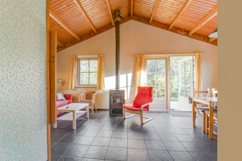 Espace de vie lumineux au Holiday Home «5 Aarde Green Camping Lage Zwaluwe» avec plafond en bois et grandes fenêtres.