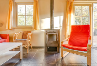 Stue med ovn, rødt stol, kurvestol og store vinduer i Holiday Home 5 Aarde Green Camping Lage Zwaluwe.