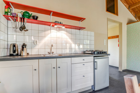 Modern kitchenette with white tiles, red shelves, and stovetop at Holiday Home 5 Aarde Green Camping Lage Zwaluwe.