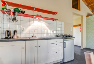 Helle Küchenzeile mit weißen Fliesen, roten Regalen und Kochfeld im Holiday Home 5 Aarde Green Camping Lage Zwaluwe.