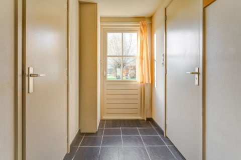 Entré i Holiday Home 5 Aarde Green Camping Lage Zwaluwe med lyse vægge, døre og vindue med gardiner.