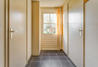 Entré i Holiday Home 5 Aarde Green Camping Lage Zwaluwe med lyse vægge, døre og vindue med gardiner.