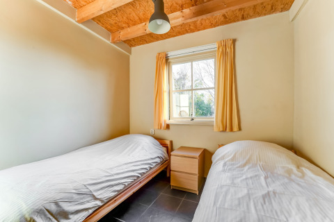 Et lyst værelse med to enkeltsenge, gule gardiner og synlige træbjælker, Holiday Home 5 Aarde Green Camping Lage Zwaluwe.