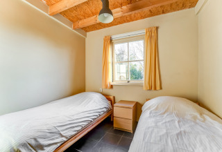 Et lyst værelse med to enkeltsenge, gule gardiner og synlige træbjælker, Holiday Home 5 Aarde Green Camping Lage Zwaluwe.