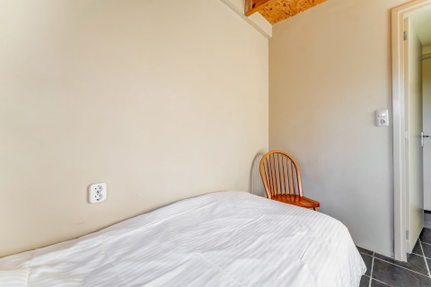 Einzelbett mit weißer Bettwäsche, Holzstuhl und schlichten Wänden im Holiday Home 5 Aarde Green Camping Lage Zwaluwe.