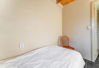 Camera semplice con letto singolo, biancheria bianca e sedia di legno presso Holiday Home 5 Aarde Green Camping Lage Zwaluwe.