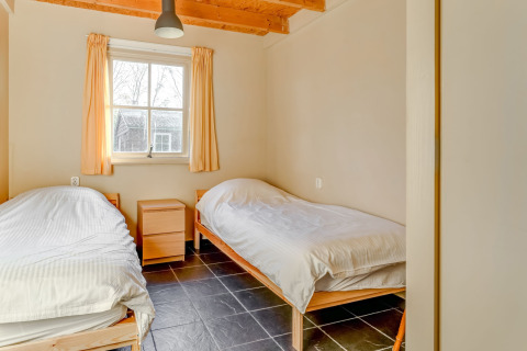 Due letti singoli in una stanza luminosa con soffitto in legno, finestra con tende e pavimento piastrellato a Holiday Home 5 Aarde Green Camping Lage Zwaluwe.