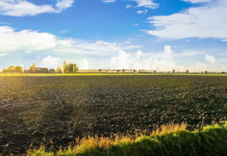 Plowed farmland under a blue sky near Holiday Home 5 Aarde Green Camping Lage Zwaluwe, Netherlands.