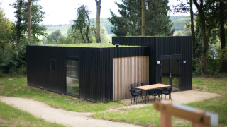 Moderne sort lodge med græs-tag og udendørs siddeplads ved Resort Gulpen 2 omgivet af natur.