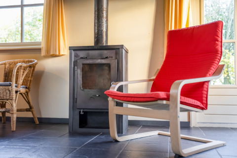 Knusse kamer in Holiday Home ‘5 Aarde Green Camping Lage Zwaluwe’ met rode stoel en houtkachel.
