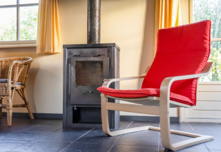 Acogedora habitación en Holiday Home «5 Aarde Green Camping Lage Zwaluwe» con silla roja y estufa.