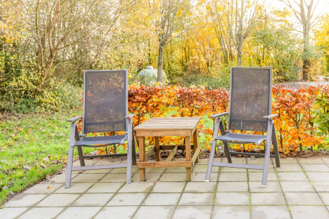 Zwei Gartenstühle und ein Holztisch auf einer Terrasse mit buntem Herbstlaub bei Holiday Home 5 Aarde Green Camping Lage Zwaluwe, Niederlande.