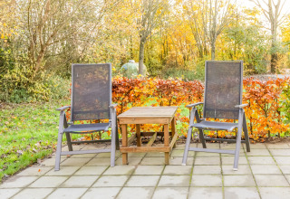 To havestole og et træbord på en fliseterrasse omgivet af efterårsløv ved Holiday Home 5 Aarde Green Camping Lage Zwaluwe i Holland.