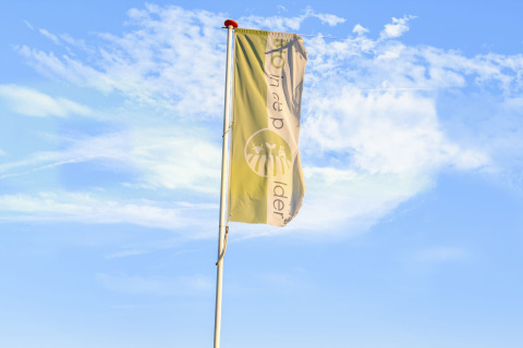 Eine Fahne weht vor blauem Himmel bei Holiday Home 5 Aarde Green Camping Lage Zwaluwe in den Niederlanden.