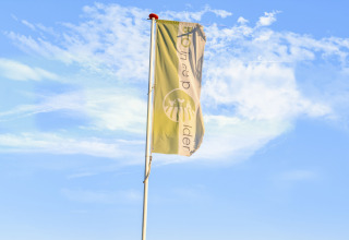 Et flag blafrer i vinden ved Holiday Home 5 Aarde Green Camping Lage Zwaluwe, Nederland, under blå himmel.
