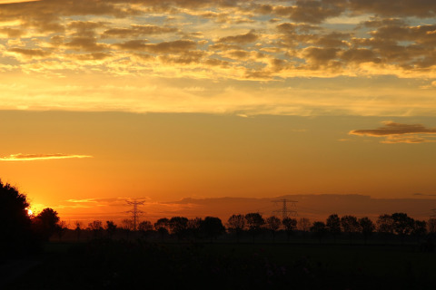 Zonsondergang aan Holiday Home 5 Aarde Green Camping Lage Zwaluwe in Nederland, met bomen en wolken aan de horizon.