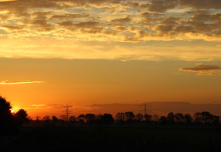 Solnedgang over landskabet ved Holiday Home 5 Aarde Green Camping Lage Zwaluwe i Holland med træer og skyer.