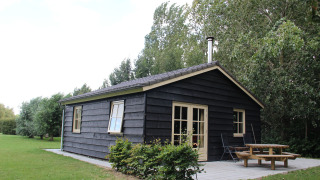 Et billede af Holiday Home 3 Aarde Green Camping Lage Zwaluwe, en sort træhytte med terrasse og have.