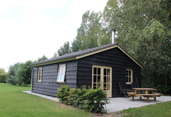 Photo of Holiday Home 3 Aarde Green Camping Lage Zwaluwe, a small black wooden lodge with a patio and trees.