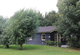 Una cabaña de madera rodeada de árboles y césped en Holiday Home 3 Aarde Green Camping Lage Zwaluwe, Países Bajos.