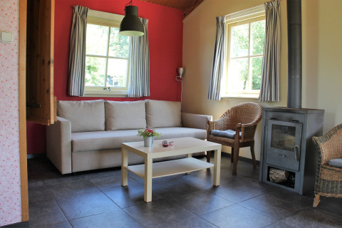 Lys stue med sofa, kurvestole, brændeovn og store vinduer i Holiday Home 3 Aarde Green Camping Lage Zwaluwe.