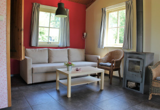 Helles Wohnzimmer mit Sofa, Korbstühlen und Holzofen im Holiday Home 3 Aarde Green Camping Lage Zwaluwe.
