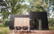 Cabaña moderna de madera negra con mesa exterior en Resort Gulpen 6, rodeada de naturaleza en los Países Bajos.