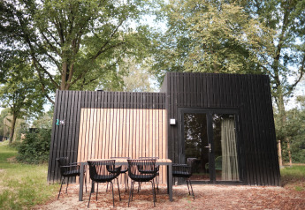 Cabaña moderna de madera negra con mesa exterior en Resort Gulpen 6, rodeada de naturaleza en los Países Bajos.