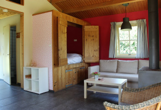 Wohnbereich im Holiday Home 3 Aarde Green Camping Lage Zwaluwe mit Sofa, Bett und Holzofen.